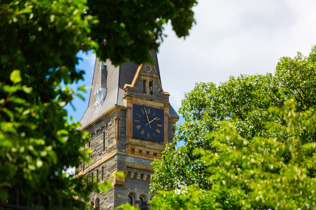 The clocktower of Healy Hall is visible through the leaves of trees.