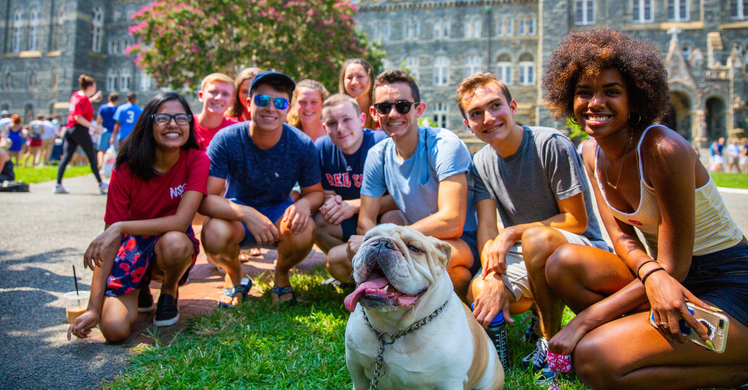 A group of students squat around Jack the Bulldog during New Student Orientation.