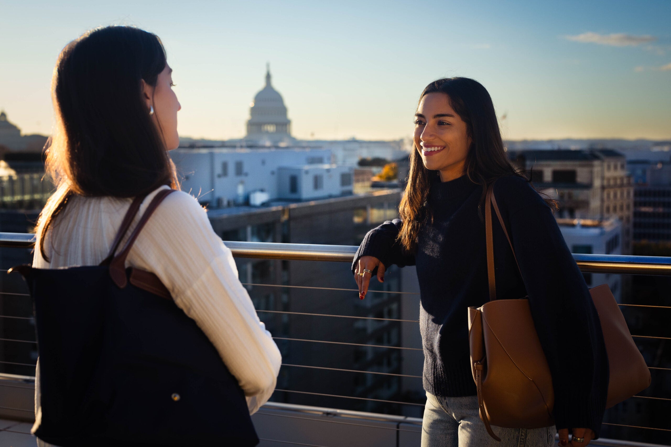 Two students talk to each other on a balcony overlooking the US Capitol Building.
