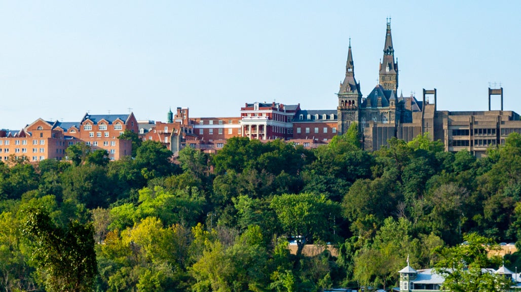 The skyline of Georgetown University, including the tops of Healy Hall and Lauinger Library, is visible on a hill above trees.