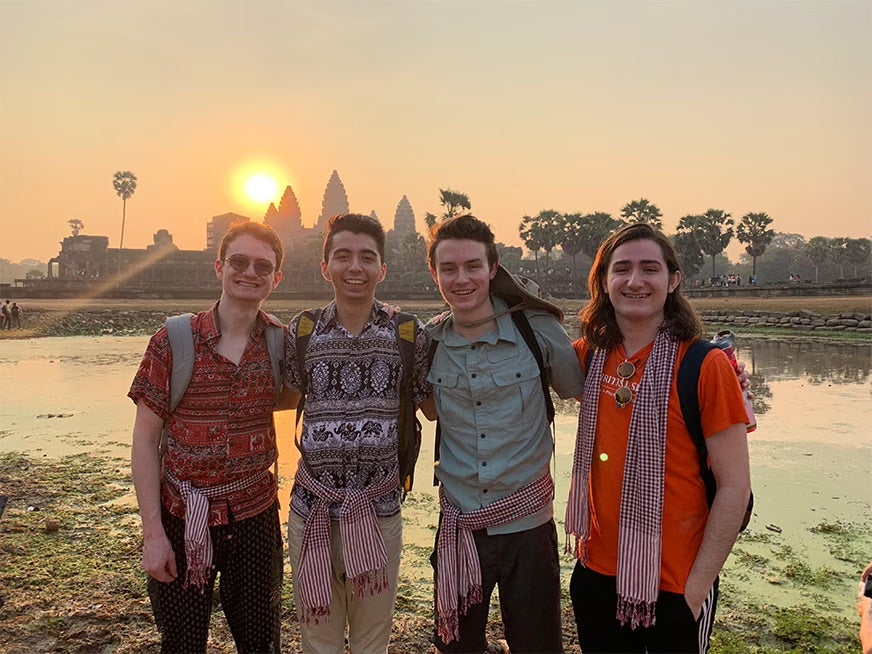 Four students stand in front of Angkor Wat and a setting sun.