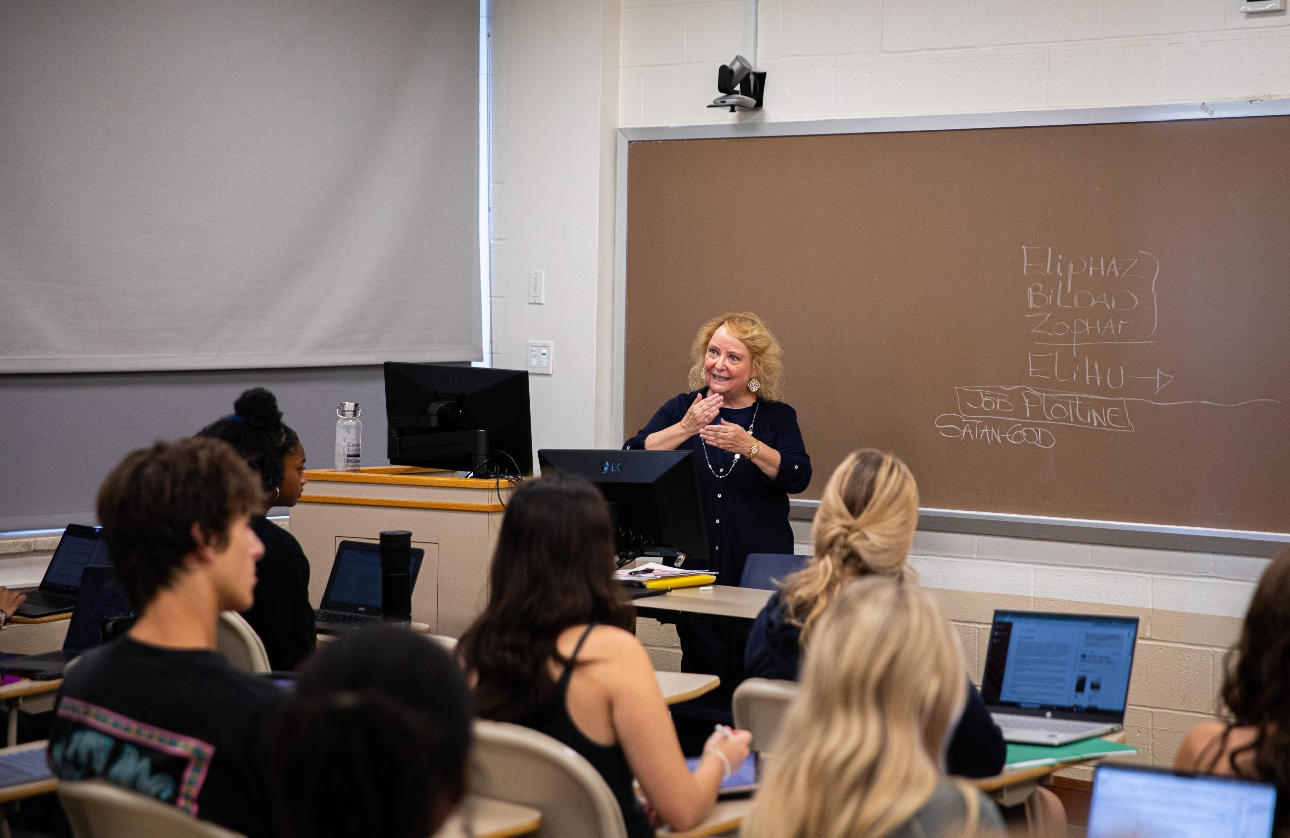A professor teaches in the front of a classroom.