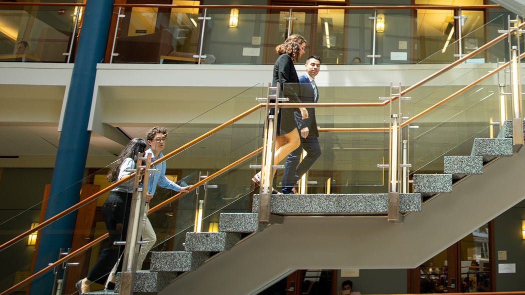 Four students in professional attire walk up a stairway within the Hariri Building.