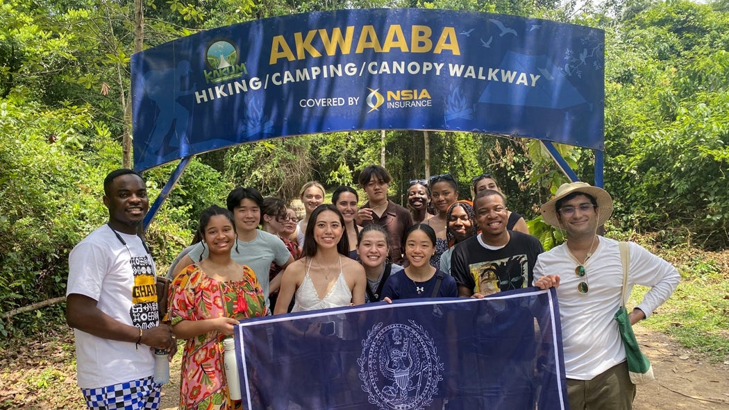 A group of students pose with a Georgetown flag in front of a sign reading