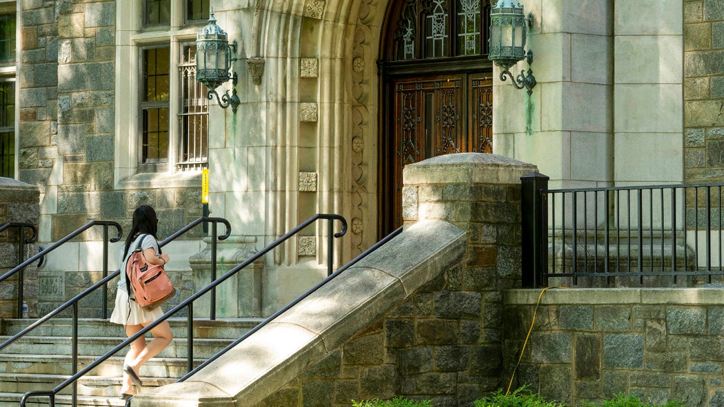 A student carrying a pink backpack walks up steps to the front entrance of Copley Hall.