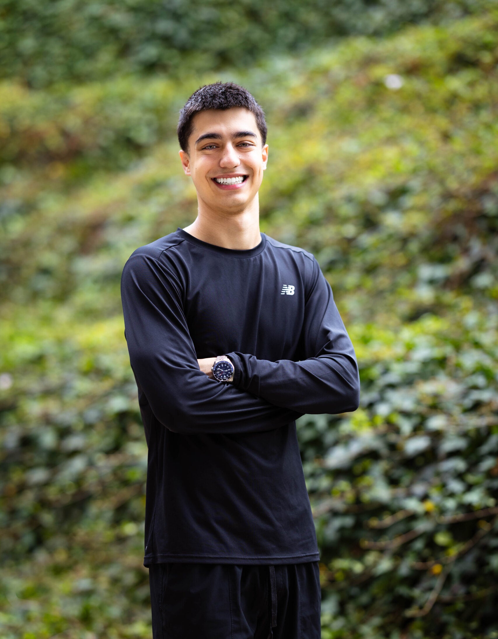 Kiumars stands in front of bushes while smiling.