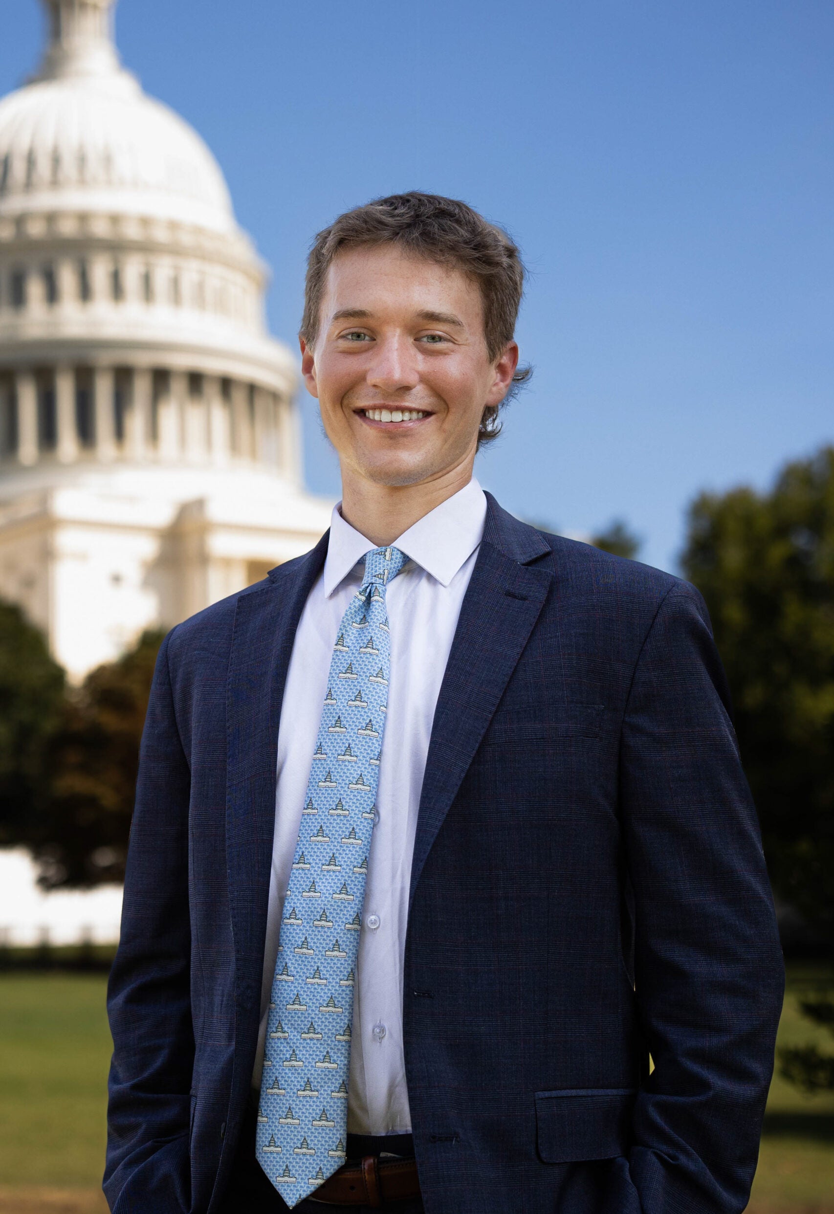 Luke stands in front of the US Capitol Building wearing a suit.