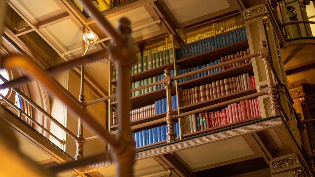 Books on an ornate bookshelf behind wrought iron railings on the upper level of Riggs Library.