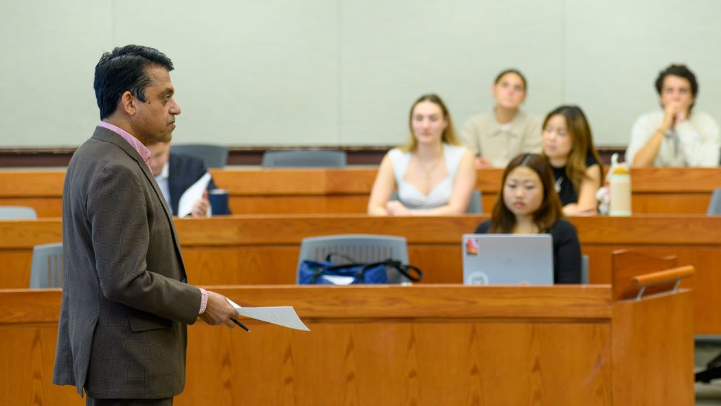 A professor teaches in the front of a classroom as students watch on.