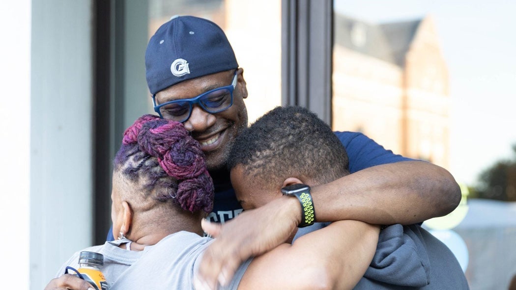 A family hugs each other during move-in at Georgetown. The father is wearing a backwards cap with a Georgetown logo on it.