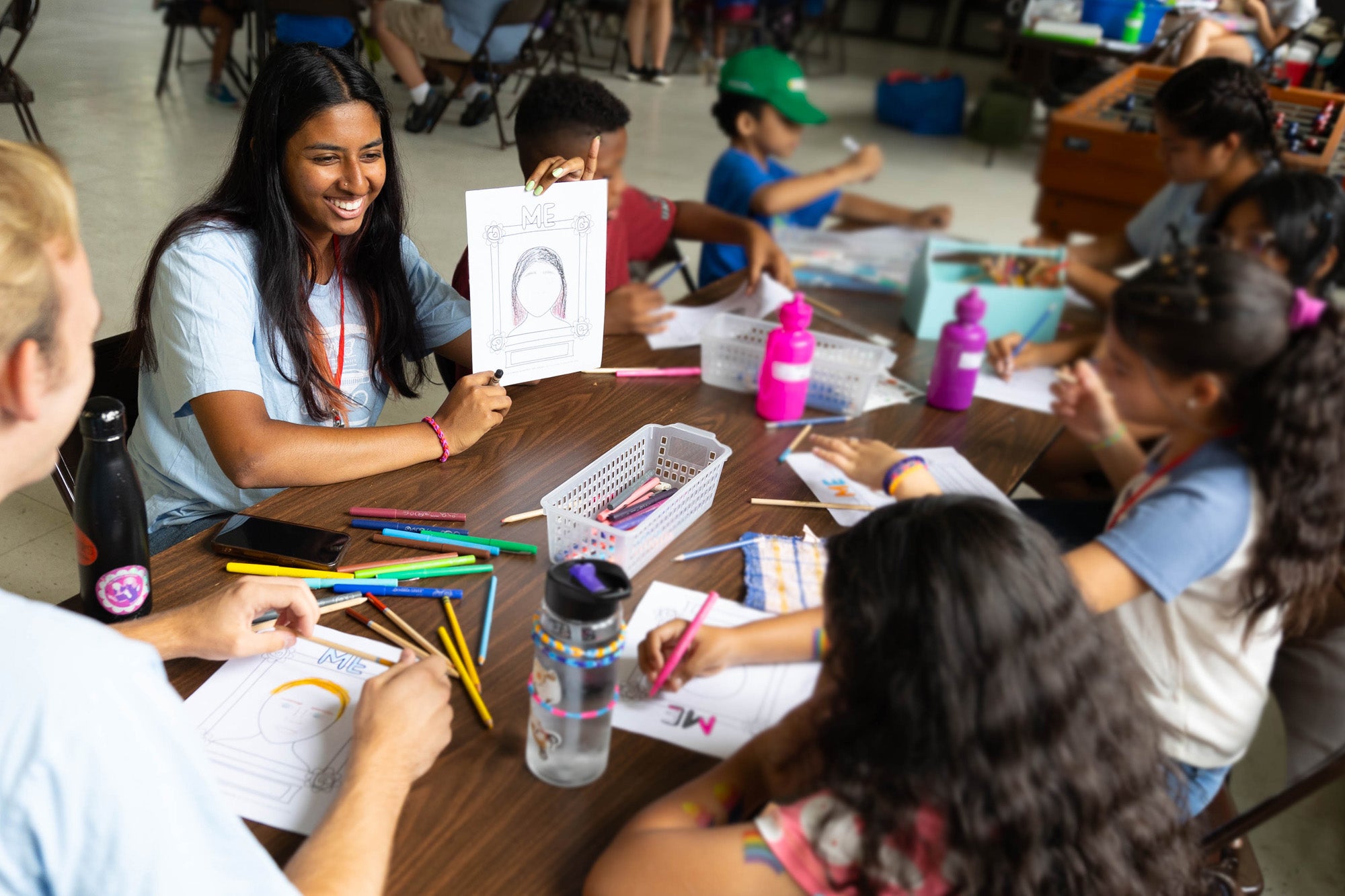 A Georgetown student shows a drawing to young children, who are also drawing with markers.