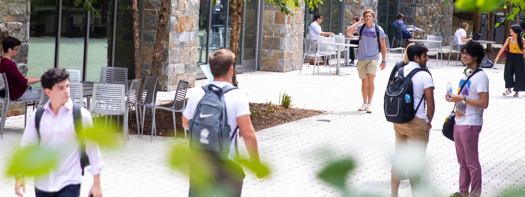 Students, most of whom are wearing backpacks, walk along a path outside of Arrupe Hall.